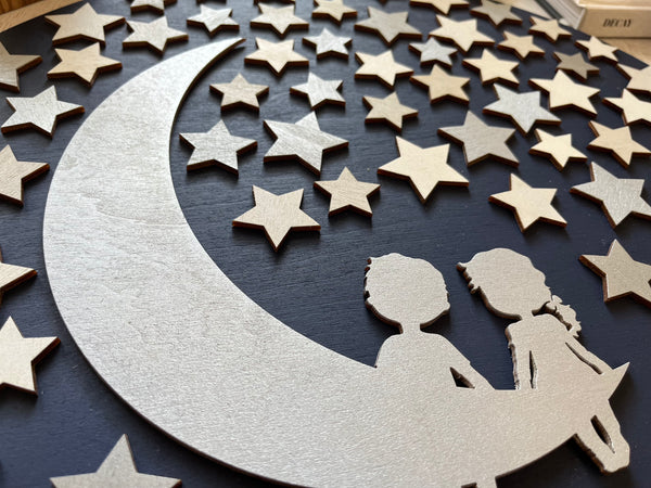 Decorative wall art with a crescent moon, stars, and silhouettes of two people against a dark background.