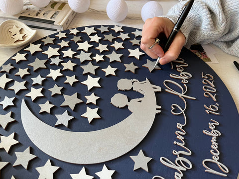 Person signing a silver star on a decorative wedding guest book alternative with stars and personalized text on a navy blue background
