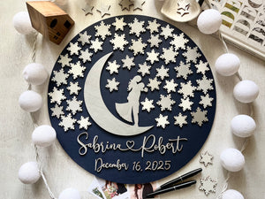 Decorative wall art guest book alternative with a silhouette of a couple on a moon, surrounded by snowflakes, on a wooden surface. Can be used as a wedding guest book for guests to sign a snowflake each.