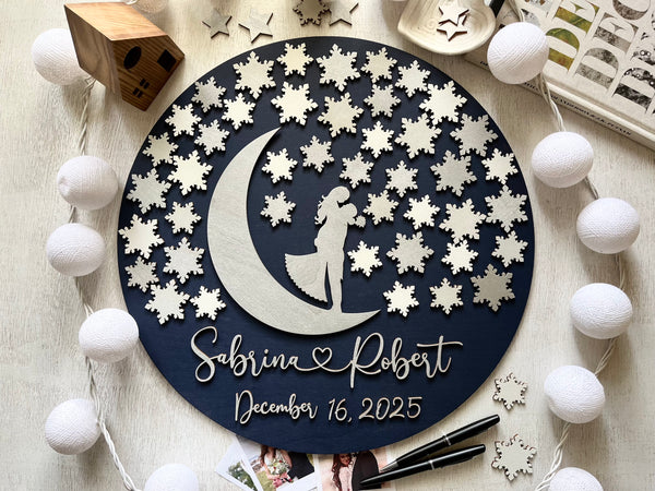 Decorative wall art guest book alternative with a silhouette of a couple on a moon, surrounded by snowflakes, on a wooden surface. Can be used as a wedding guest book for guests to sign a snowflake each.