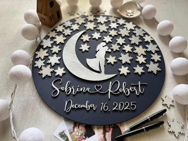 Decorative wall art guest book alternative with a silhouette of a couple on a moon, surrounded by snowflakes, on a wooden surface. Can be used as a wedding guest book for guests to sign a snowflake each.