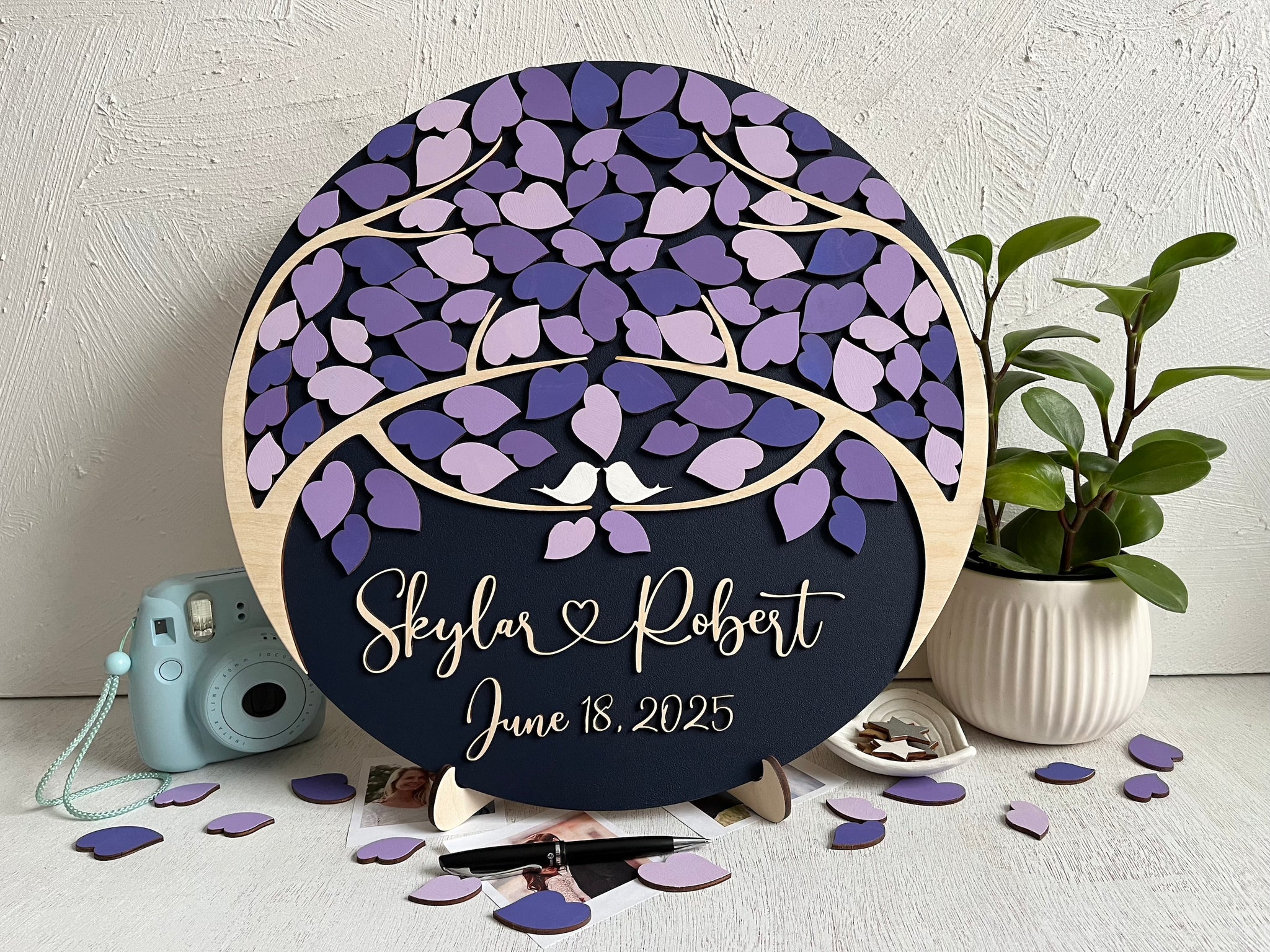 Decorative wedding guest book with purple leaf design and personalized text on a magnetic wooden surafce with removable magnetic leaves in purple, lavender, violet shades. Each guest signs a leaf and the round guest book can be hung in your home as a wedding memento. 