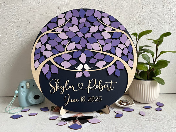 Decorative wedding guest book with purple leaf design and personalized text on a magnetic wooden surafce with removable magnetic leaves in purple, lavender, violet shades. Each guest signs a leaf and the round guest book can be hung in your home as a wedding memento. 
