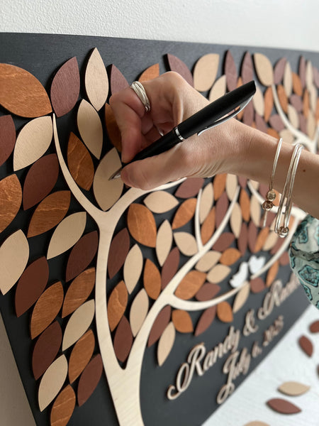 hand signing a leaf on a 3D guest book alternative personalized for wedding or anniversary