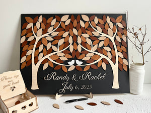 Personalized wedding guest book with magnetic removable leaves- each guest signs one leaf for the board. The board is rectangular, made with two trees that come into one, with the names of the bride and groom underneath and wedding date in script lettering. There is a box for storing leaves. 