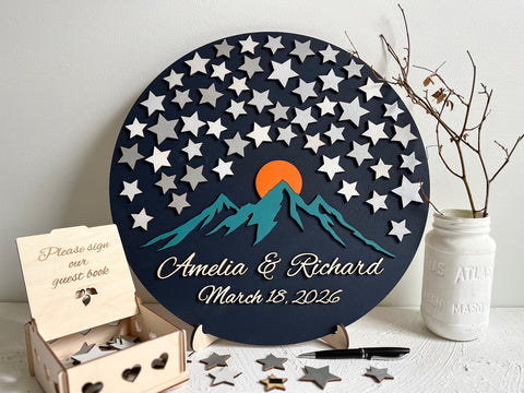 Round wedding guest book alternative with star pattern, mountains, and personalized text displayed on a wooden stand. The guest book board is magnetic and the stars can be removed and added or rearranged on the board. 