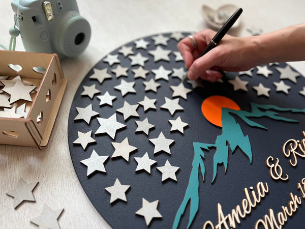 Hand using a pen to sign star-shaped pieces on a 3D wood wedding guest book alternative personalized with the names f the bride and groom