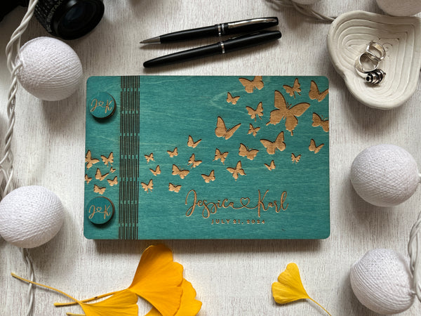 wood guest book for signing personalized with the names of the bride and groom and butterflies flying away on a teal stained wood