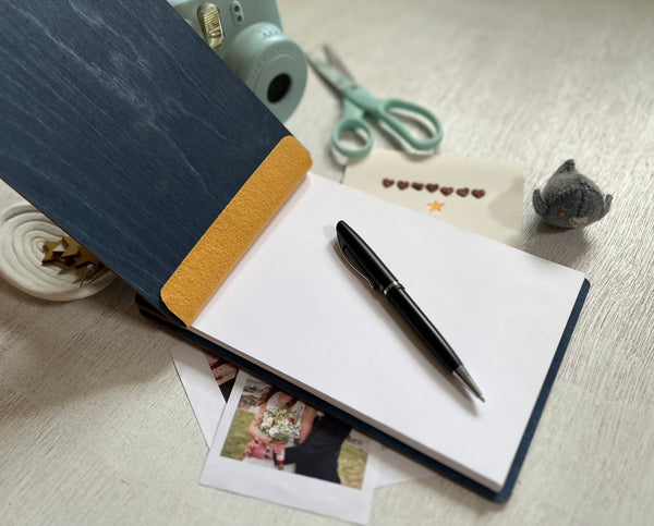 Open notebook with a pen on a light surface, surrounded by stationery items. The guest book can be used for a wedding or bridal shower with engraved personalized names and text