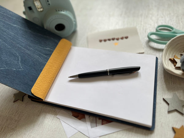Pen on a notebook with stationery items on a wooden surface
