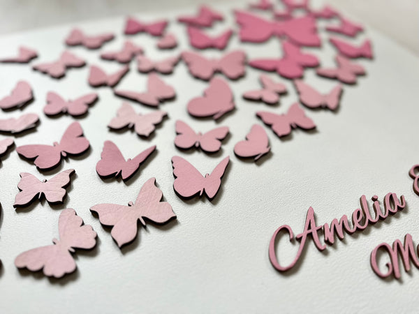 Butterfly wedding guest book with personalized names and date on a wood white board shown- closeup to show the pink ombre effect