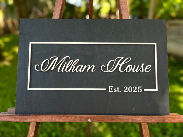 Black plaque with personalized name and established date - text in gold on a black background shown in a graden wedding setting