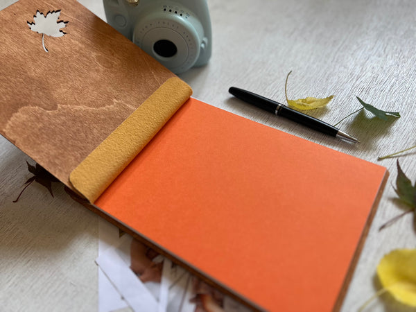 Open notebook with brown cover and orange accent, pen, and camera on a light surface.
