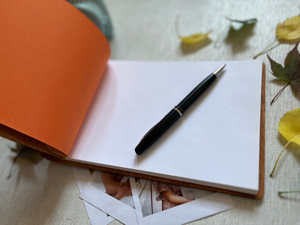 Pen on a notebook with leaves and photos in the background