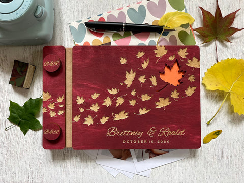 Personalized guest book with wooden covers and autumn maple  leaf design with  engraved text on a burgundy stain wooden surface.