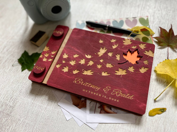 Personalized guest book with wooden covers and autumn maple  leaf design with  engraved text on a burgundy stain wooden surface.