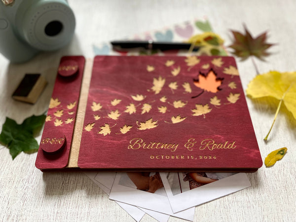 Personalized guest book with wooden covers and autumn maple  leaf design with  engraved text on a burgundy stain wooden surface.