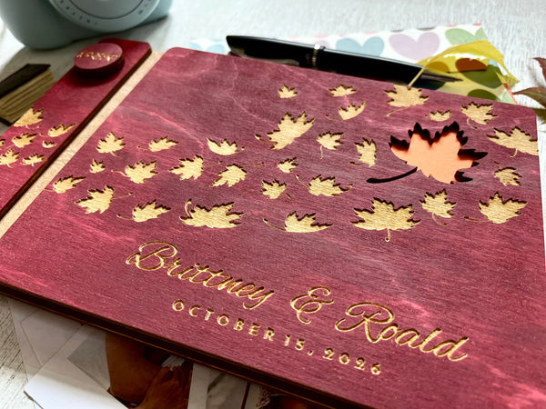 Personalized guest book with wooden covers and autumn maple  leaf design with  engraved text on a burgundy stain wooden surface.