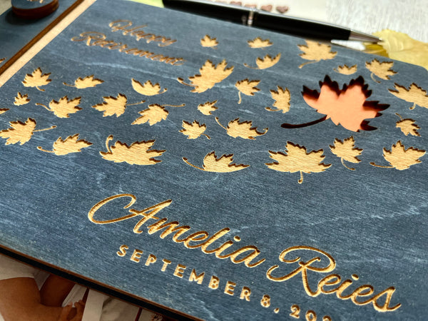 Personalized retirement guest book with autumn leaf design on a custom engraved surface with maple leaves and  personalized with the name of the retiree and the text "Happy Retirement"