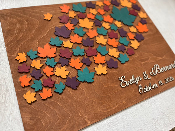 Wooden board with colorful maple leaf-shaped cutouts and personalized  names and date- used as a wedding guest book alternative for guest signatures