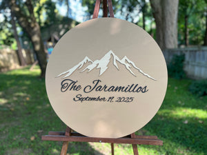 Round decorative plaque with mountain design and text on a stand personalized with a last name and wedding date