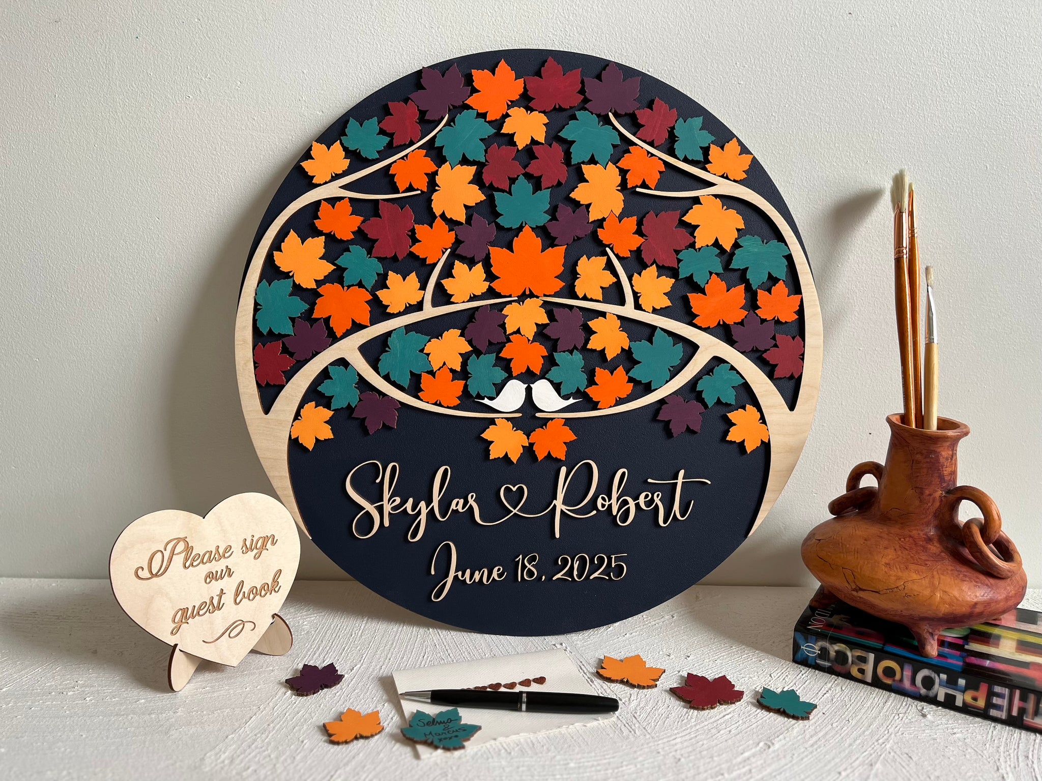 Decorative wedding guest book with colorful maple leaf design and personalized text on a round wooden board.