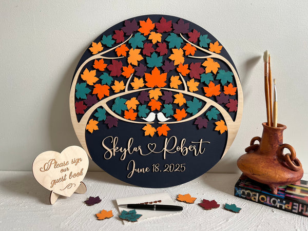 Decorative wedding guest book with colorful maple leaf design and personalized text on a round wooden board.