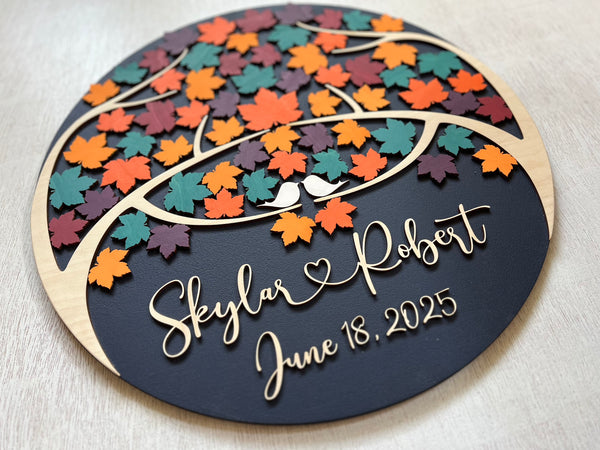 Decorative wedding guest book with colorful maple leaf design and personalized text on a round wooden board.