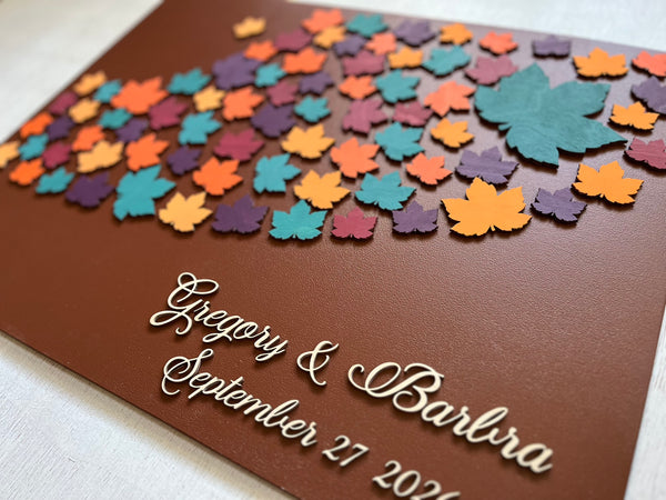 Decorative magnetic guest book with colorful leaf patterns and personalized text on a brown background with maple leaves. Each leaf is magnetic and can be signed and added to the background.