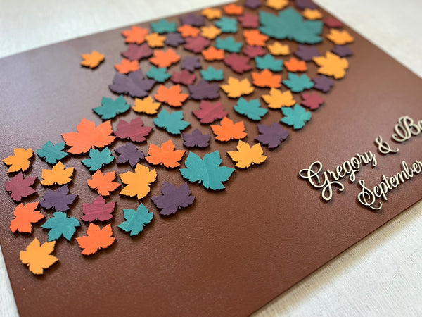 Decorative magnetic guest book with colorful leaf patterns and personalized text on a brown background with maple leaves. Each leaf is magnetic and can be signed and added to the background.