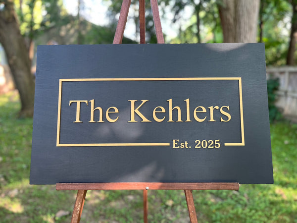 Decorative sign with personalized last name and established year with gold text - shown on a stand outdoors.