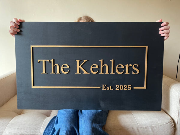 Person holding a sign with custom last name and established date 