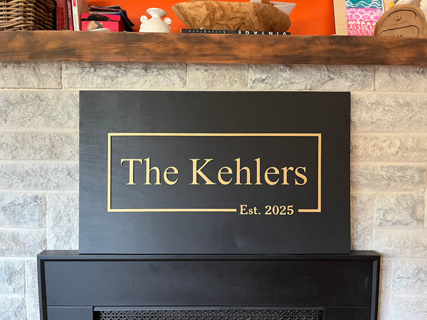 Personalized fireplace sign with last name and established date in golden text shown on a stone wall background.