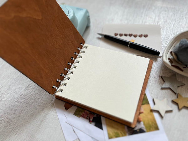 Open notebook with spiral binding, pen, and photos on a light surface