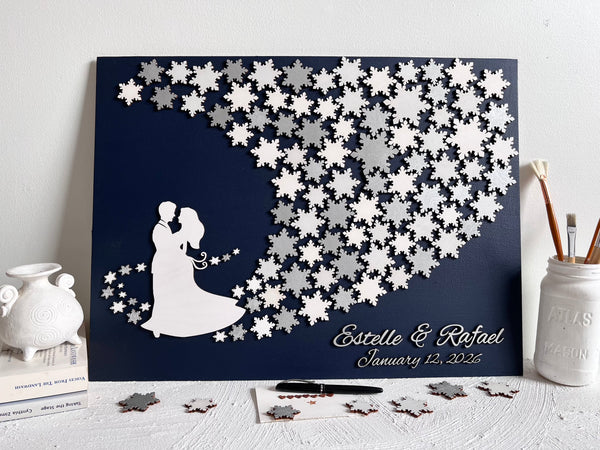 Wedding guest book wall art with snowflakes to sign, personalized names, wedding date and silhouettes of a couple on a navy blue background. 