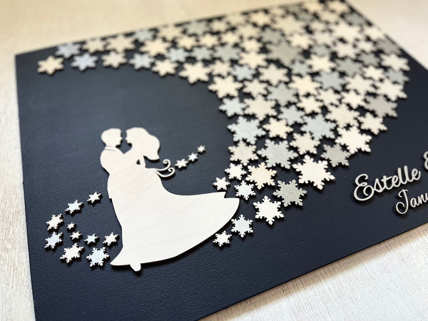 Wedding guest book wall art with snowflakes to sign, personalized names, wedding date and silhouettes of a couple on a navy blue background. 