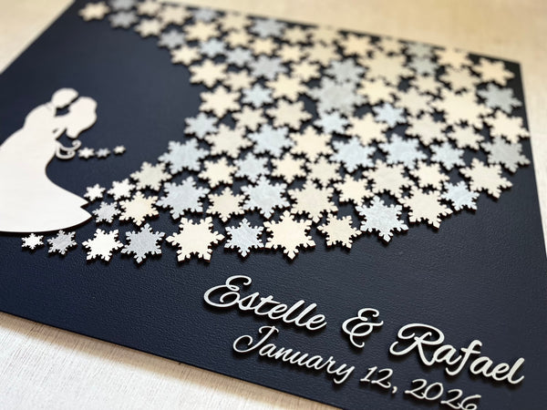 Wedding guest book wall art with snowflakes to sign, personalized names, wedding date and silhouettes of a couple on a navy blue background. 