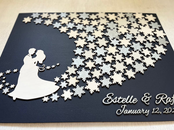 Wedding guest book wall art with snowflakes to sign, personalized names, wedding date and silhouettes of a couple on a navy blue background. 