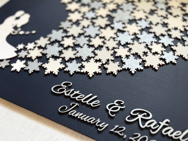 Wedding guest book wall art with snowflakes to sign, personalized names, wedding date and silhouettes of a couple on a navy blue background. 