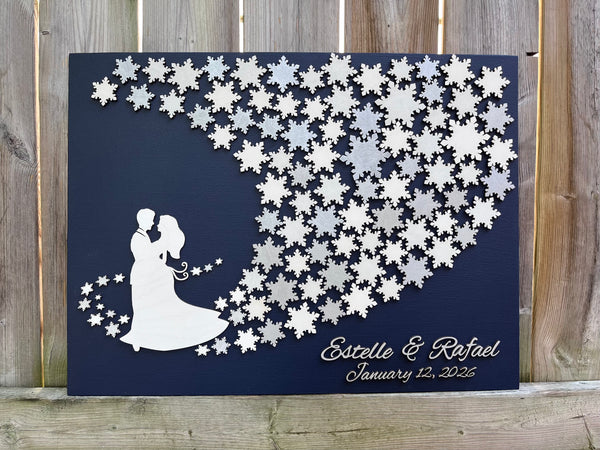 Wedding guest book wall art with snowflakes to sign, personalized names, wedding date and silhouettes of a couple on a navy blue background. 
