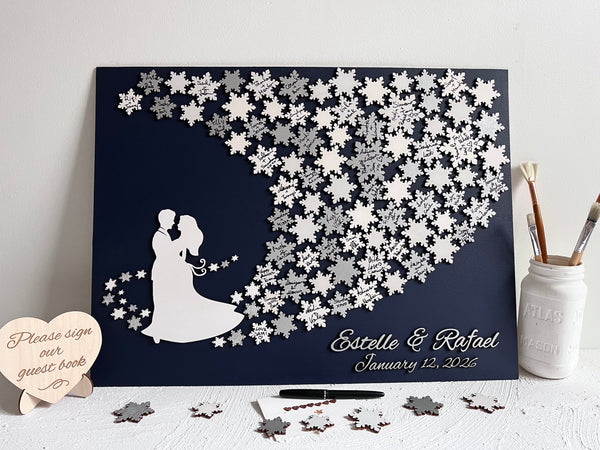 Wedding guest book wall art with snowflakes to sign, personalized names, wedding date and silhouettes of a couple on a navy blue background. 