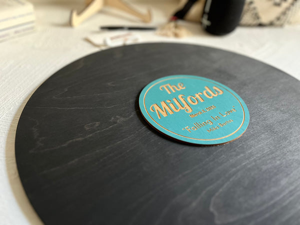 Vinyl music record lookalike sign used as a wedding guest book with personalized names, date and special song title and artist engraved in the middle. The wedding guests sign the record 