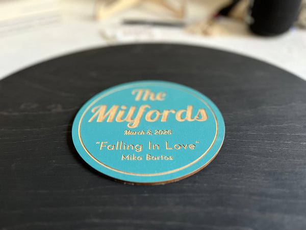 Vinyl music record lookalike sign used as a wedding guest book with personalized names, date and special song title and artist engraved in the middle. The wedding guests sign the record 