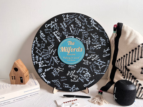 Vinyl music record lookalike sign used as a wedding guest book with personalized names, date and special song title and artist engraved in the middle. The wedding guests sign the record 