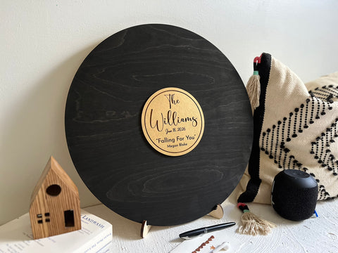 Round black wooden music record used as a wedding guest book for guest signatures. Personalized with the last name of the couple, a wedding date as well as a favourite song and artist, engraved in the middle of the record, to mimic a musical vinyl record.