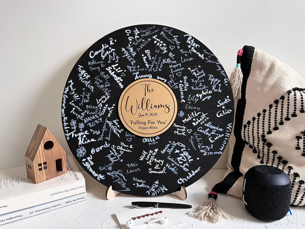 Round black wooden music record used as a wedding guest book for guest signatures. Personalized with the last name of the couple, a wedding date as well as a favourite song and artist, engraved in the middle of the record, to mimic a musical vinyl record.