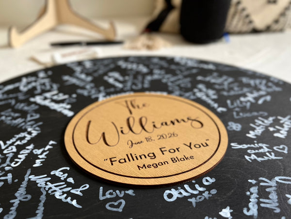 Round black wooden music record used as a wedding guest book for guest signatures. Personalized with the last name of the couple, a wedding date as well as a favourite song and artist, engraved in the middle of the record, to mimic a musical vinyl record.