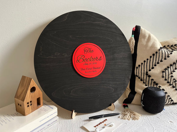 Vinyl music record lookalike sign used as a wedding guest book with personalized names, date and special song title and artist engraved in the middle. The wedding guests sign the record 
