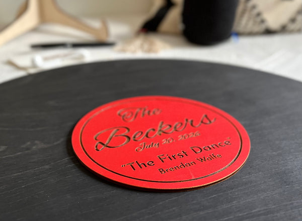 Vinyl music record lookalike sign used as a wedding guest book with personalized names, date and special song title and artist engraved in the middle. The wedding guests sign the record 