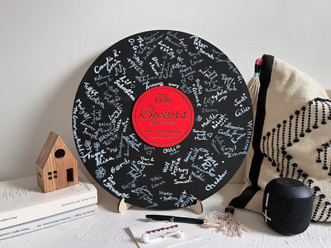 Vinyl music record lookalike sign used as a wedding guest book with personalized names, date and special song title and artist engraved in the middle. The wedding guests sign the record 